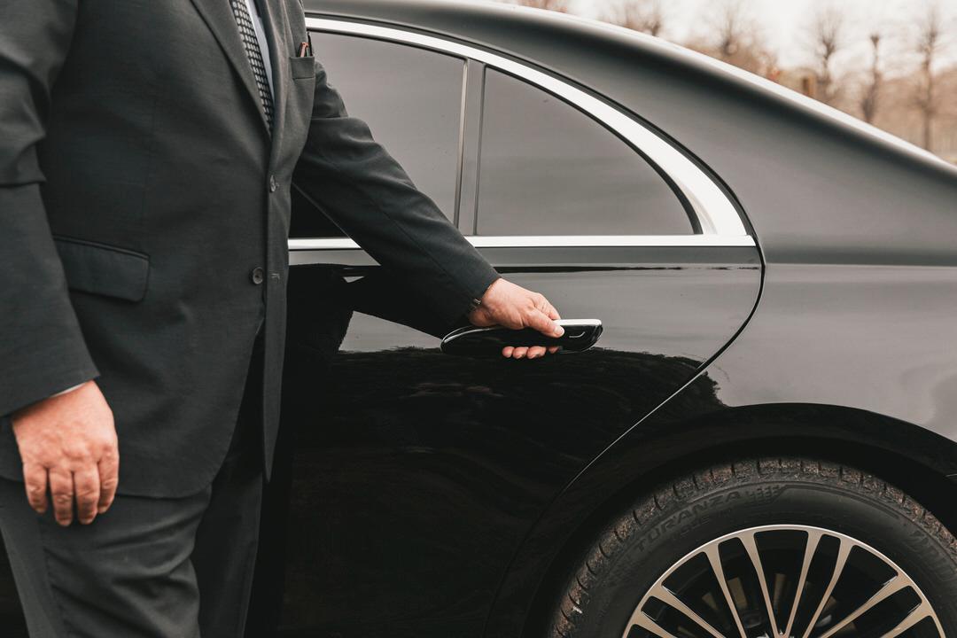 Driver holds open the door of a Mercedes S-class.